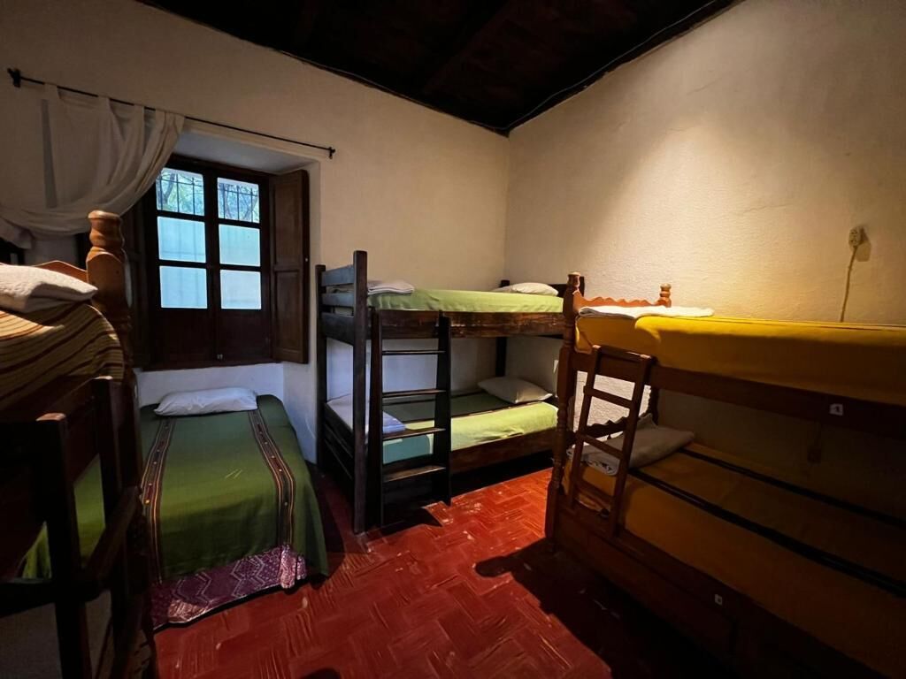 A dormitory room with bunk beds, a wooden chair, and a window with curtains.