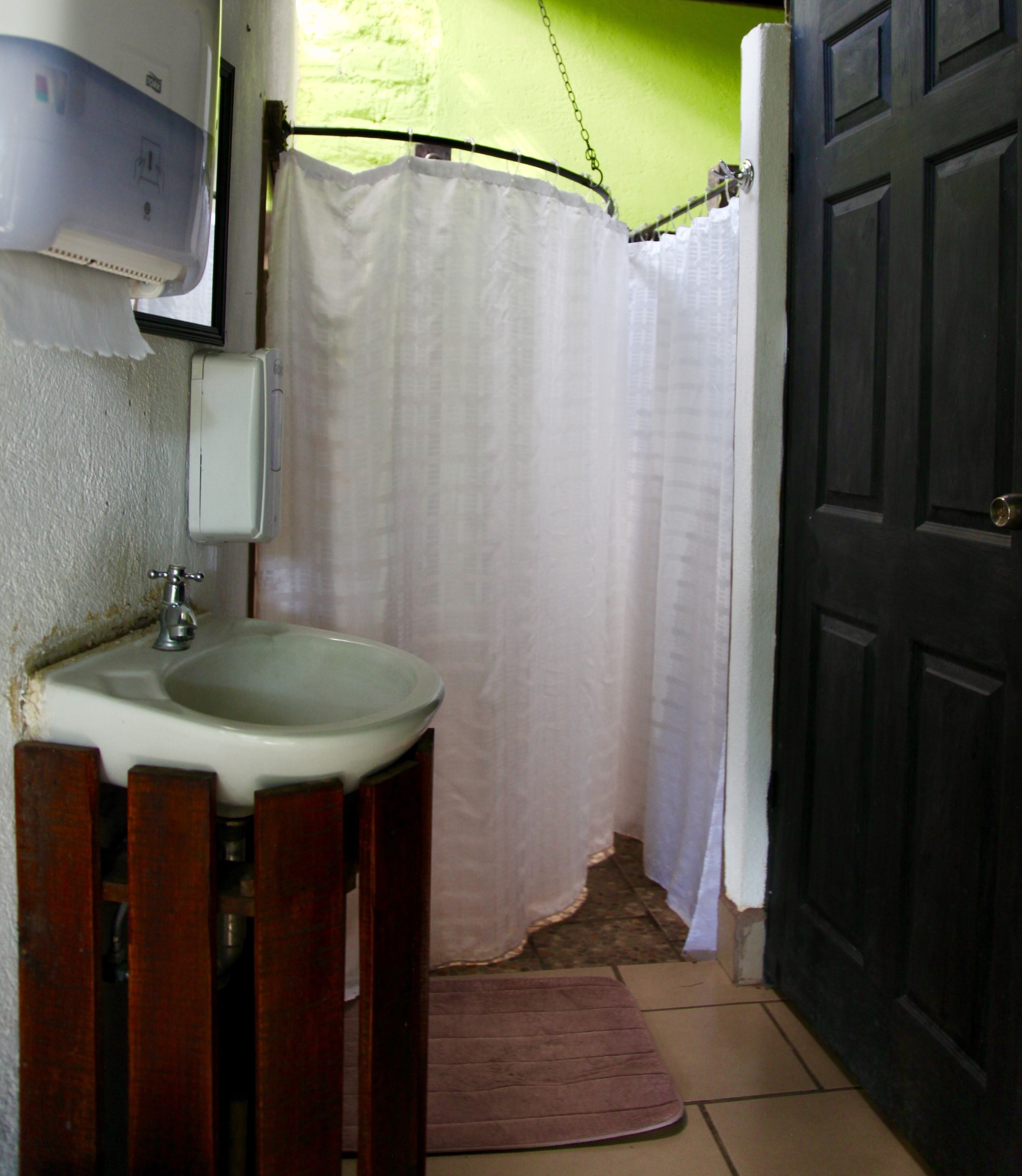 Een badkamer met een wastafel, douchegordijn en een deur.