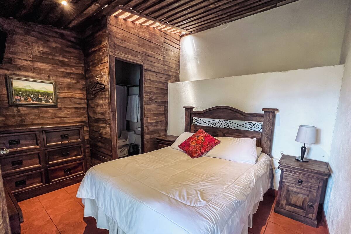 Une pièce en bois comprenant un lit, une table de chevet, une commode et une porte donnant sur une salle de bain.