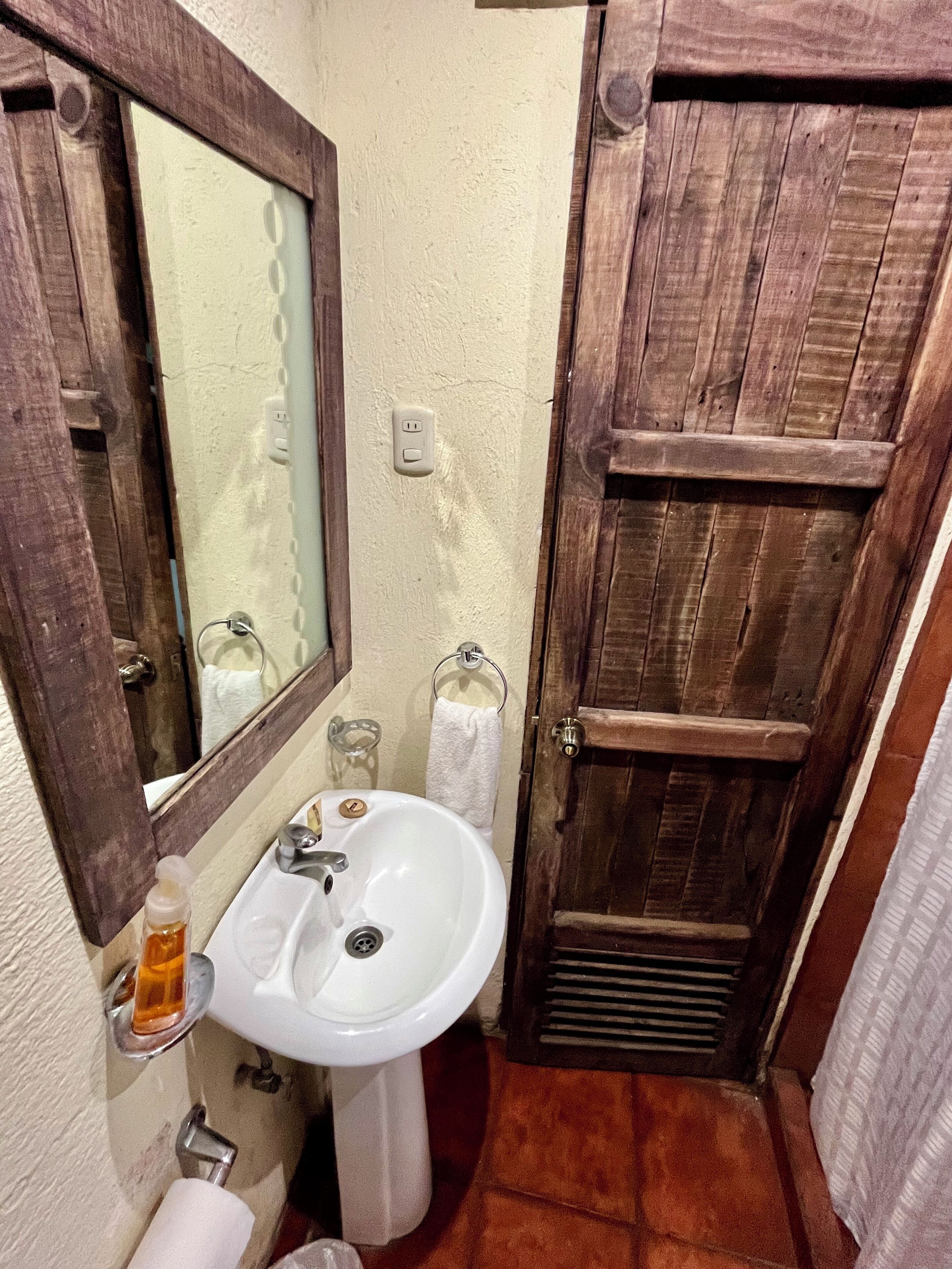 A bathroom with a wooden door, a white sink, a mirror, and a towel rack.