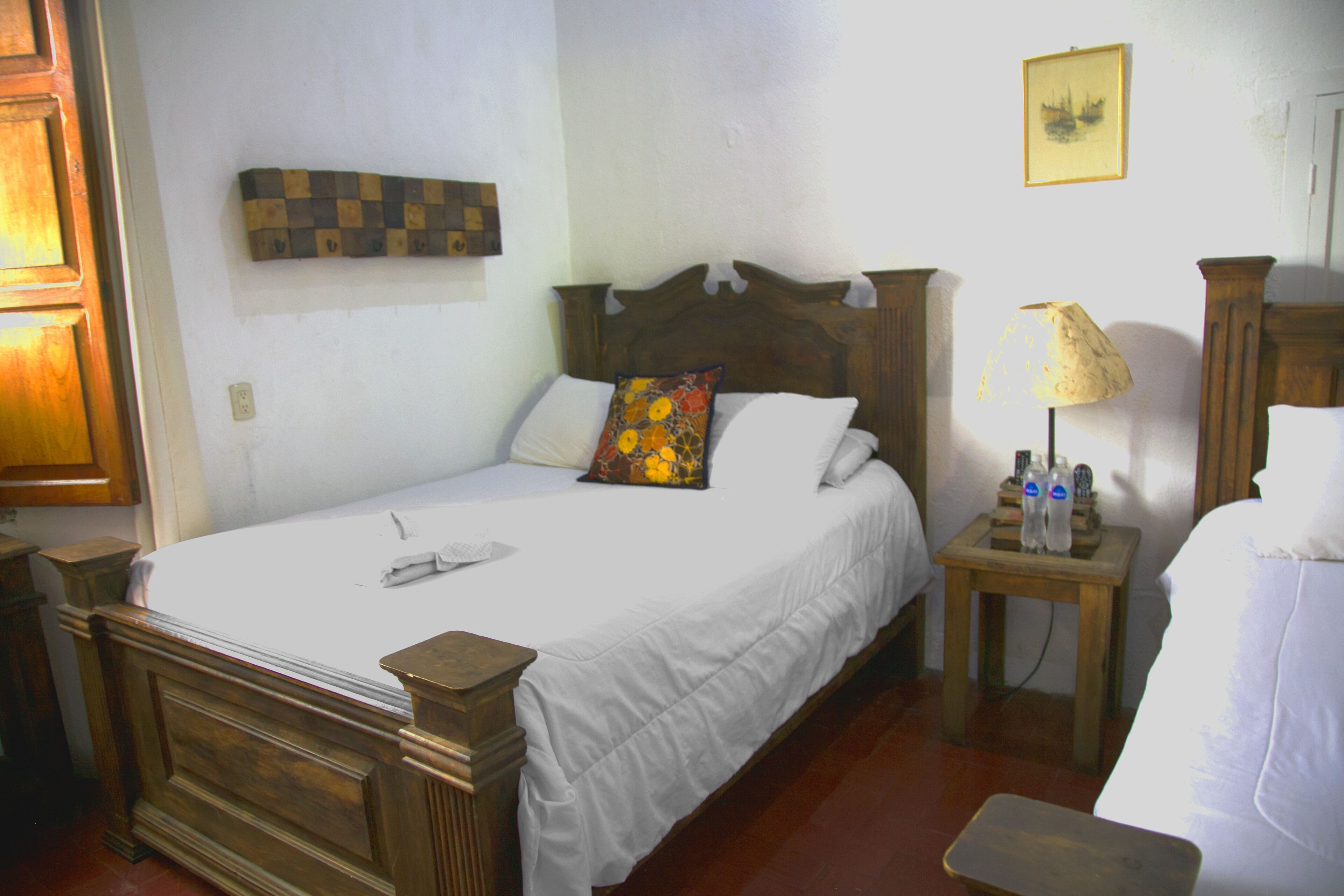 A neatly made bed with white linens and a wooden headboard, a small bedside table with a lamp, and a wall-mounted artwork above the bed.