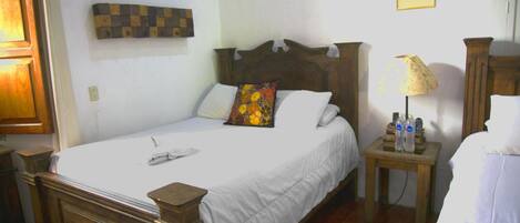 A neatly made bed with white linens and a wooden headboard, a small bedside table with a lamp, and a wall-mounted artwork above the bed.