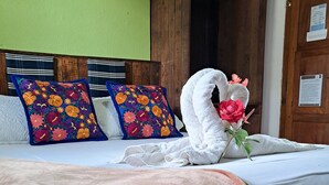 A neatly made bed with a brown bedspread, floral pillows, and a white towel shaped like a swan with a rose. - Hostal Antigueño - Hostel (Antigua Guatemala)