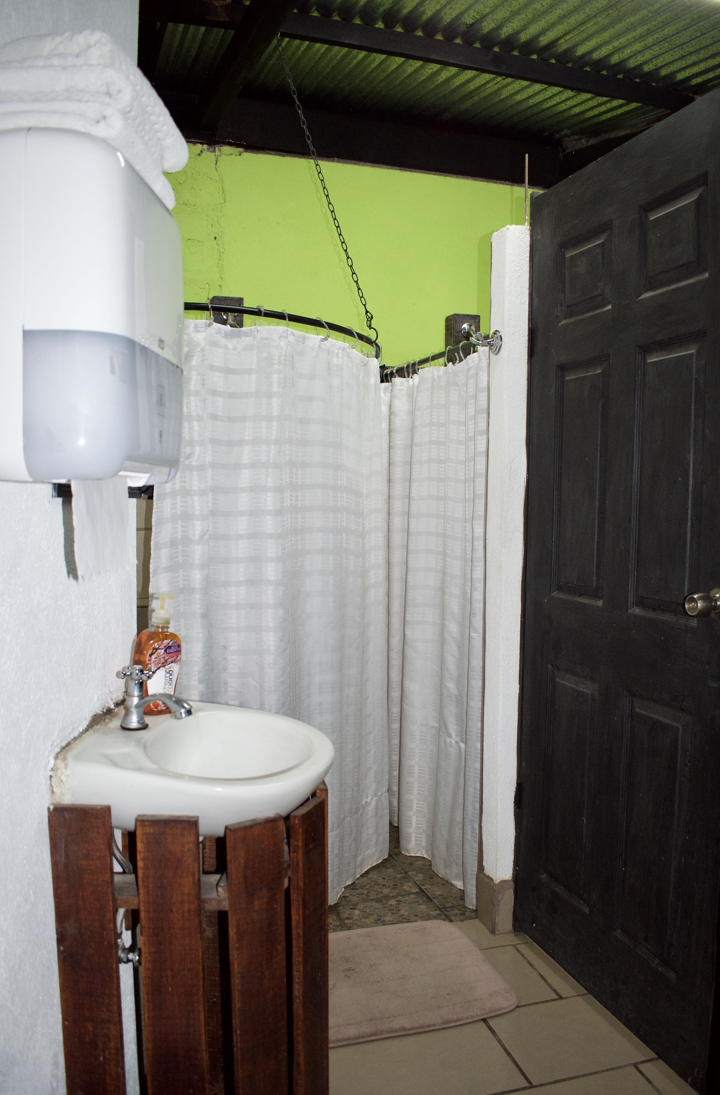 A bathroom with a white sink, a wooden chair, a shower curtain, and a dark door.