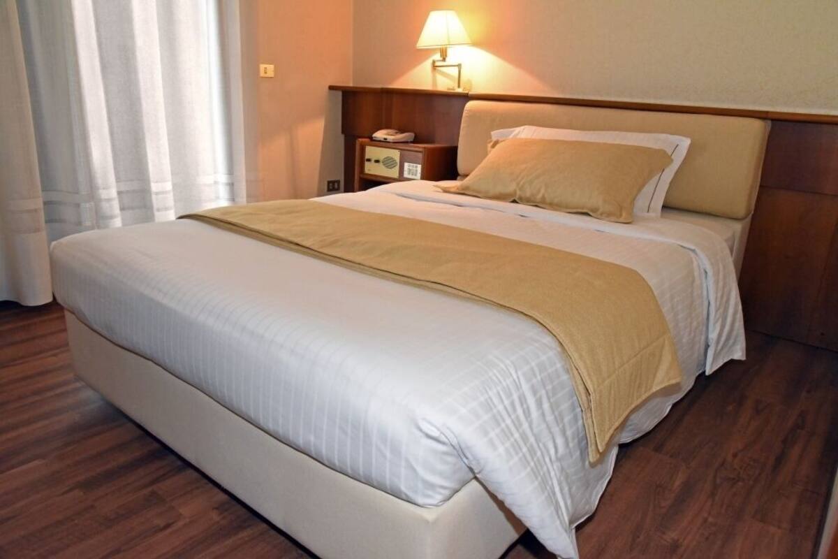 A neatly made bed with a beige blanket, a bedside table with a lamp, and a wooden headboard.