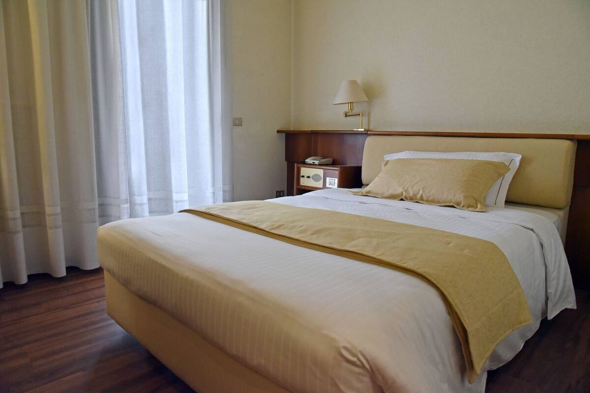 A hotel room with a large bed, a bedside table with a lamp, and a window with curtains.