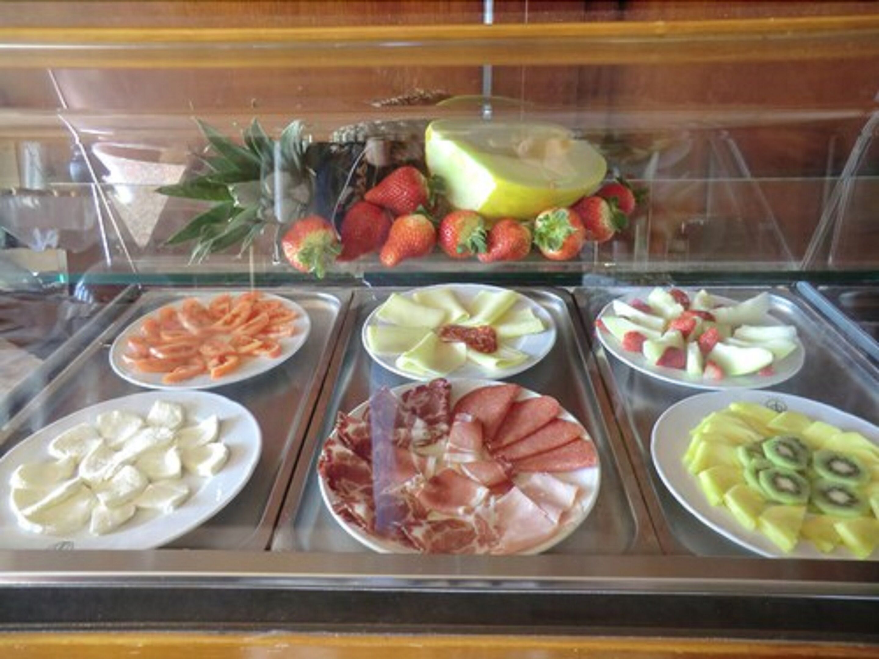 Una vitrina con diversas frutas y quesos, entre ellos fresas, kiwi y jamón.