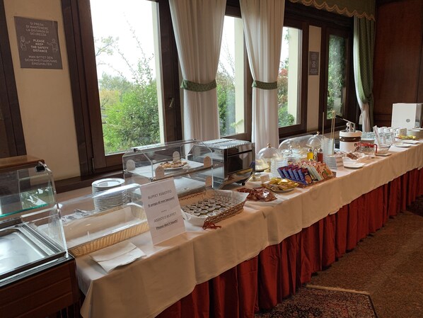 A buffet setup with various food items and a sign indicating an assisted buffet.