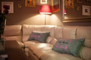 A beige leather sofa with two pillows, one with "Artistic" embroidered, and a red lamp on a table. - Art Rustic Hotel (Chisinau)