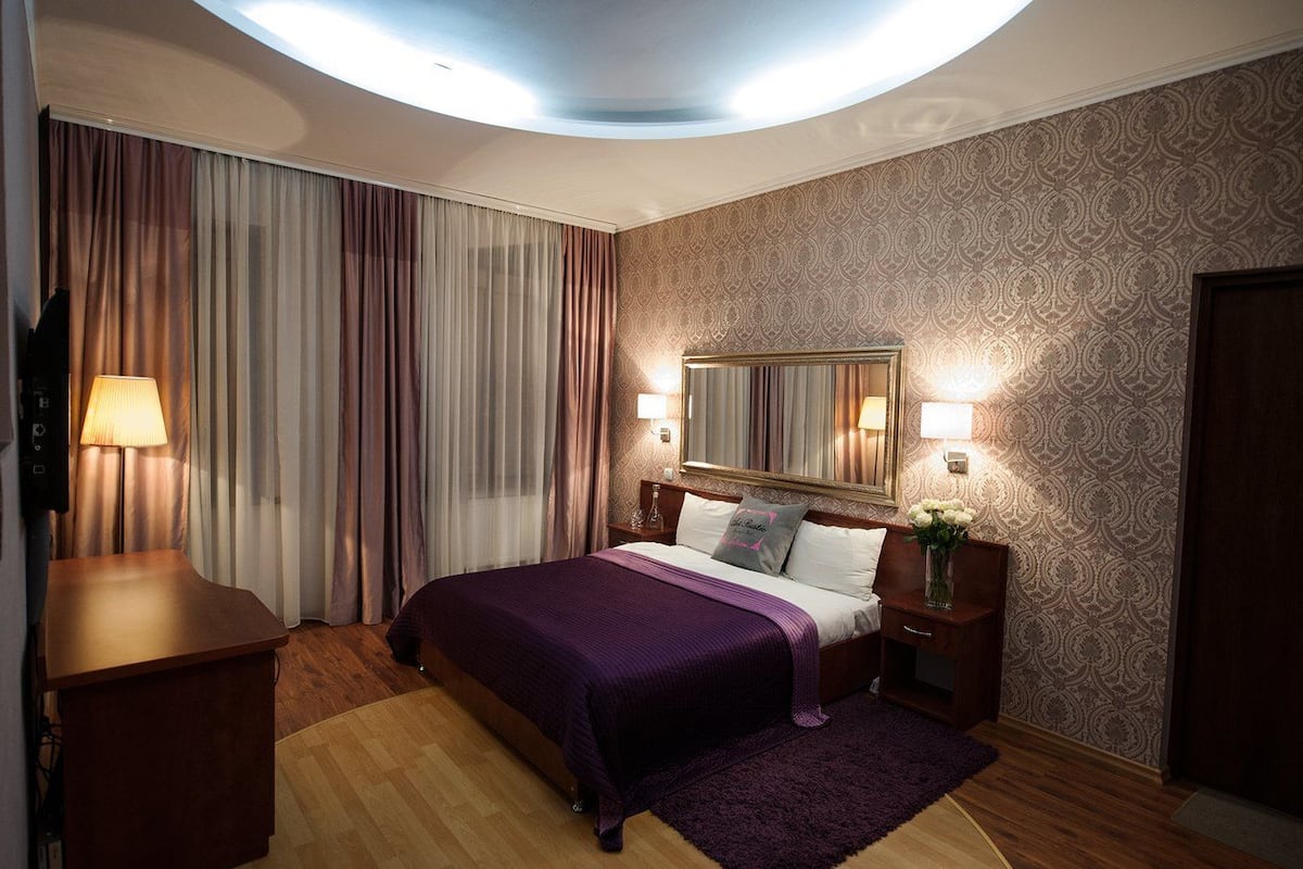 Una habitación de hotel con una cama, una mesita de noche, un escritorio, una lámpara y un espejo.