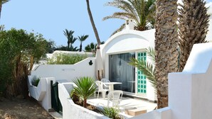 A white building with a patio area, including a table and chairs, surrounded by plants and palm trees. - Sangho Club Zarzis (Zarzis)