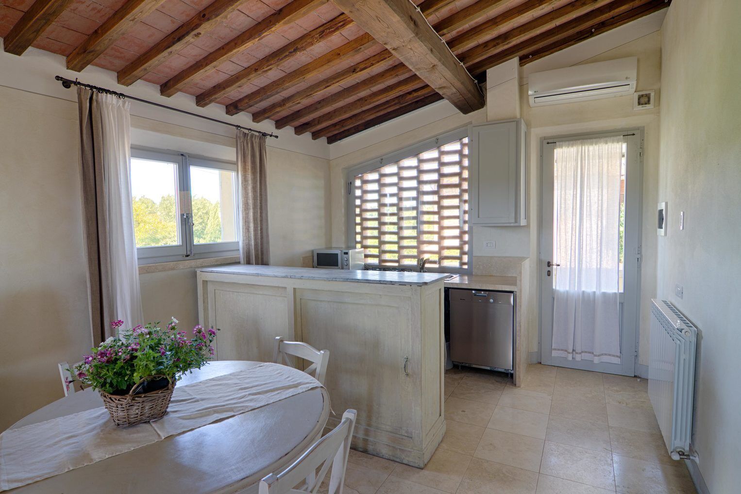 Una cocina compacta con una isla central, una mesa de comedor con sillas y una ventana con cortinas.