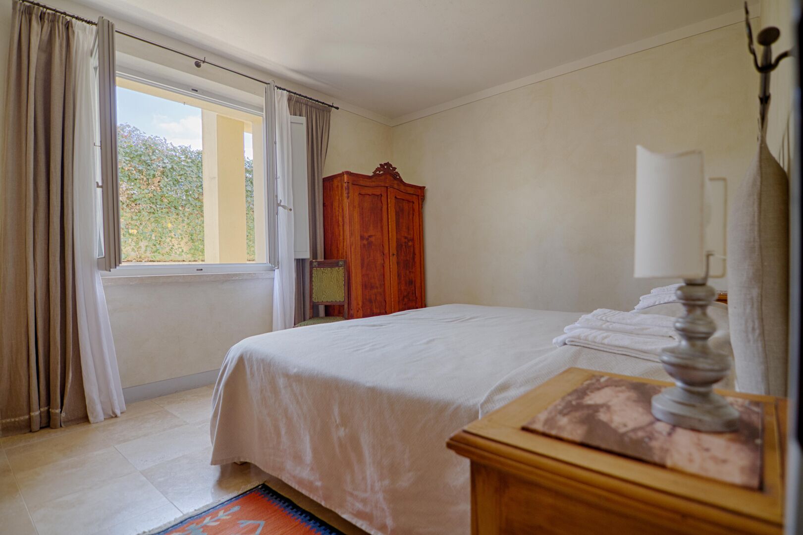 Ein Schlafzimmer mit einem Bett, einem Holzschrank, einem Nachttisch mit Lampe und einem Fenster mit Vorhängen.