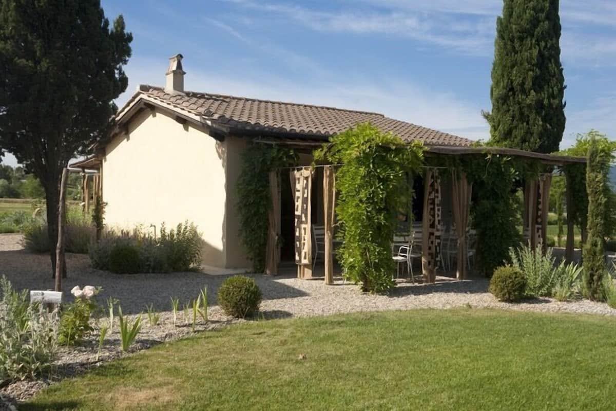 A single-story house with a tiled roof, a covered porch with a wooden railing, and a garden with various plants and a small table.
