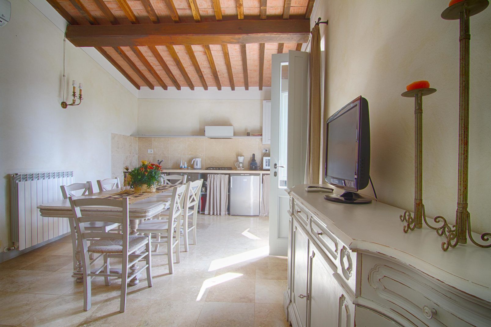 Une cuisine avec un coin repas, des poutres en bois au plafond, un téléviseur et un meuble agrémenté d’une poignée décorative.