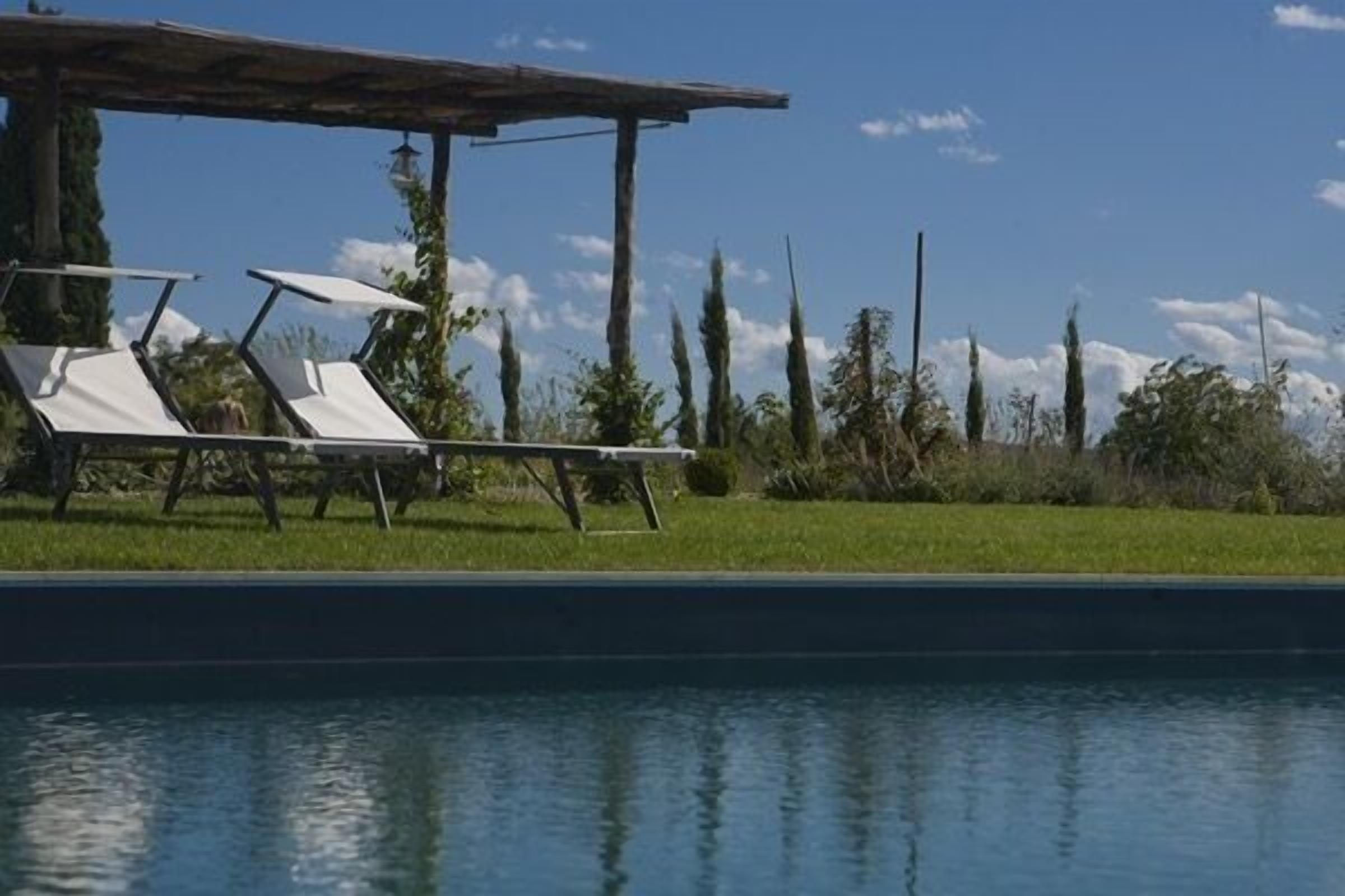 Un área de piscina con sillones de descanso y una pérgola.