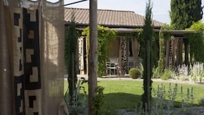 A garden with a pergola, a patio with chairs, and a tiled roof structure.