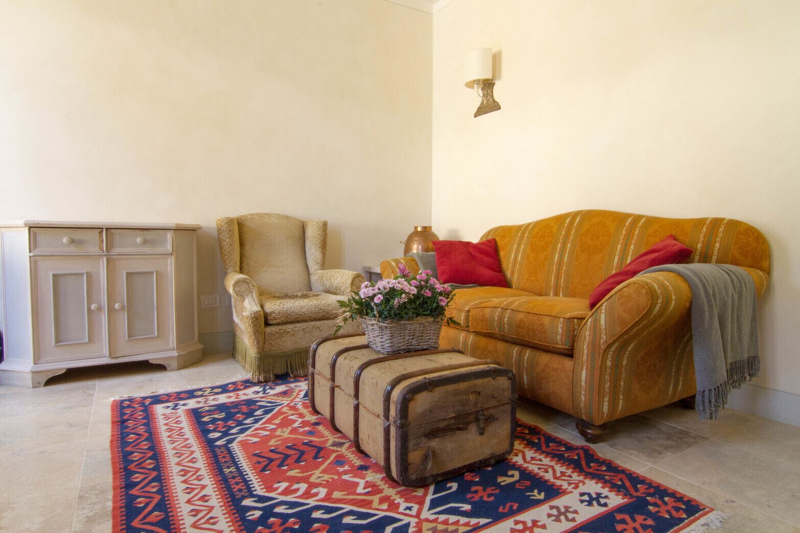Ein gemütliches Wohnzimmer mit einem gemusterten Teppich, einem alten Sessel, einer Couch mit Überwurfdecke und einem Schrank.