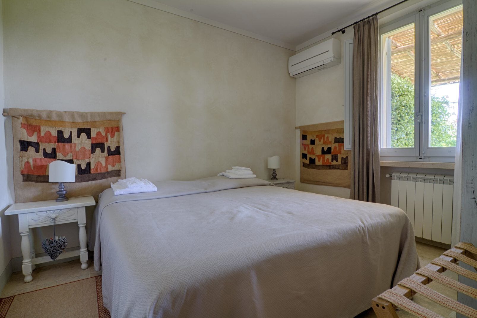 A hotel room with a large bed, a bedside table with a lamp, a window with curtains, and a radiator.