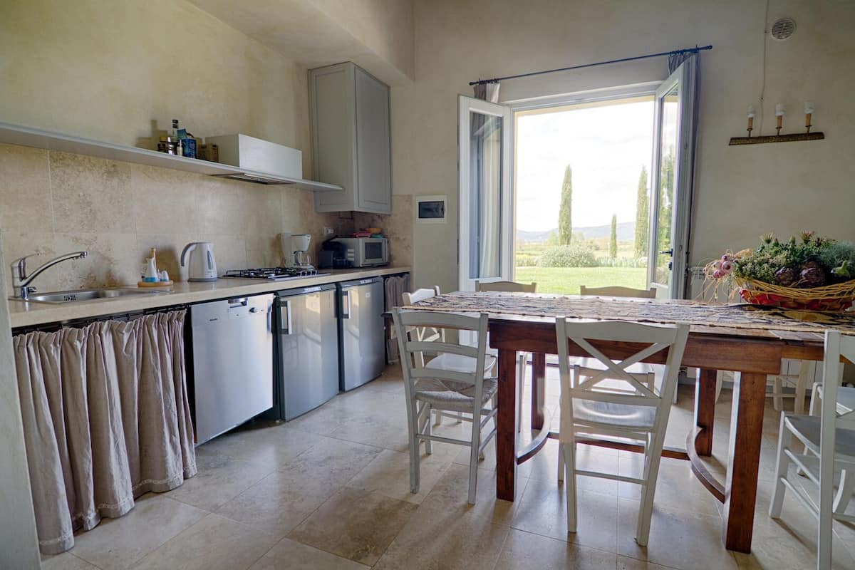 A compact kitchen with a dining area, a built-in oven, and a view through an open window.
