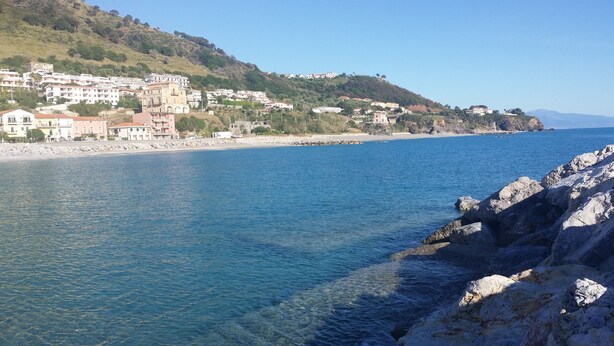 A coastal town with buildings along the shoreline, clear blue water, and rocky cliffs. - B&B Villa Betta (Bonifati)