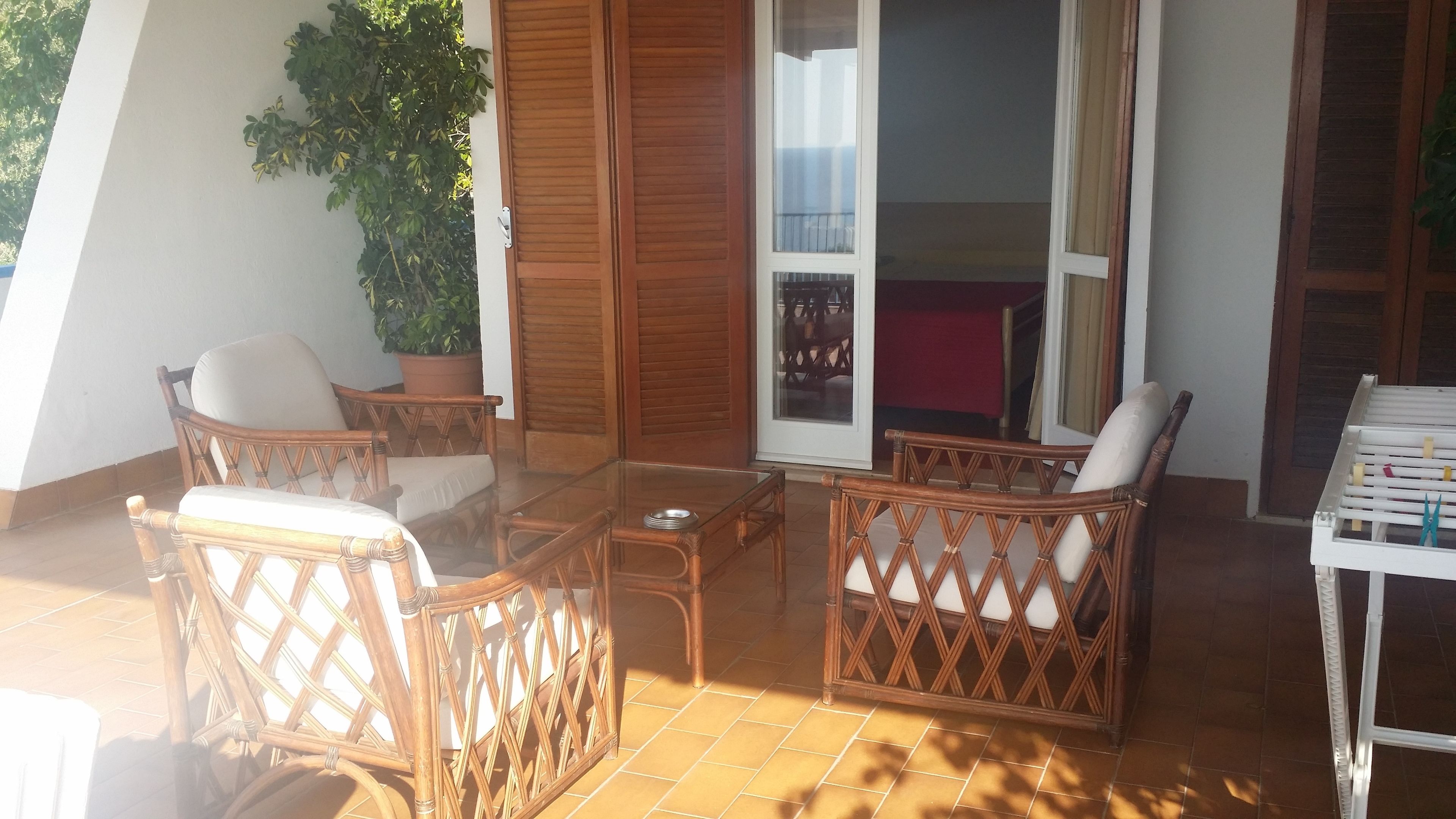 Eine sonnendurchflutete Terrasse mit Korbmöbeln, einem Glastisch und einer Schiebetür zum Balkon.