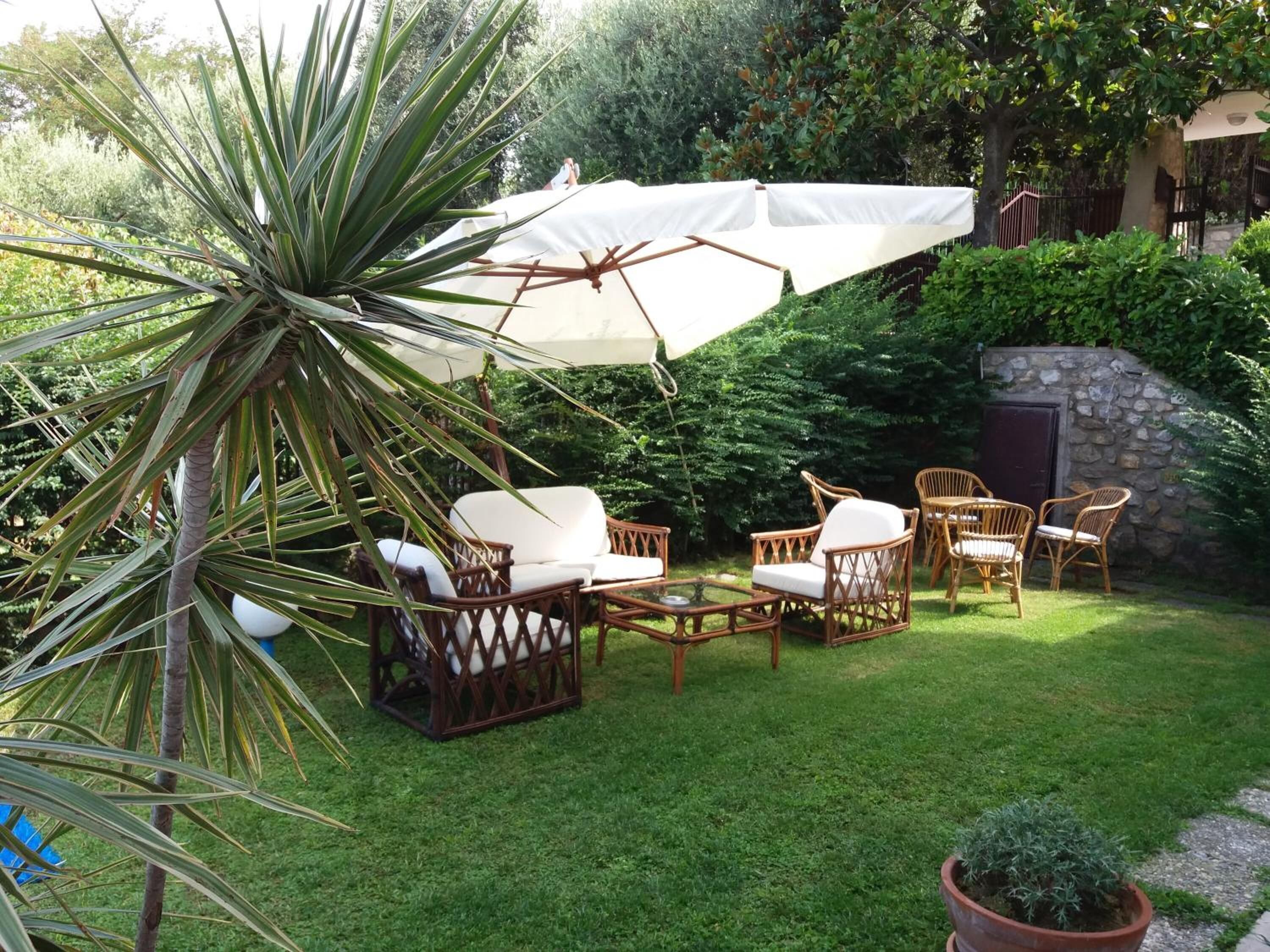 A patio area with wicker furniture, a white umbrella, and a stone wall.