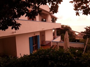 A two-story building with a balcony, a small outdoor seating area, and a view of the sea. - B&B Villa Betta (Bonifati)