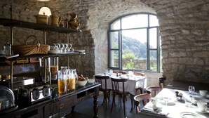 Una cocina rústica con paredes de piedra, un ventanal grande y un comedor con sillas y mesas de madera.