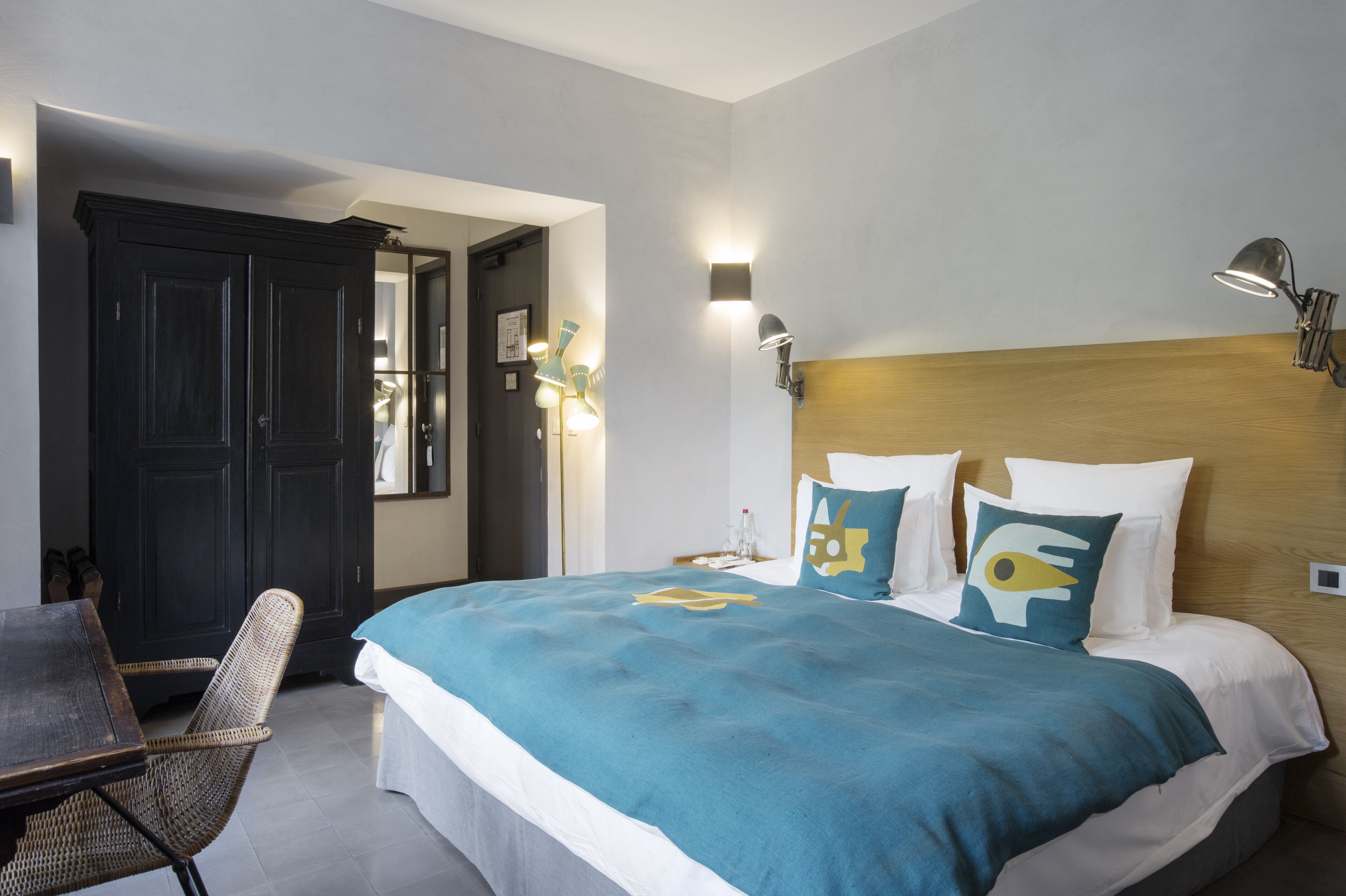 A hotel room with a bed, a chair, a desk, and a wardrobe.