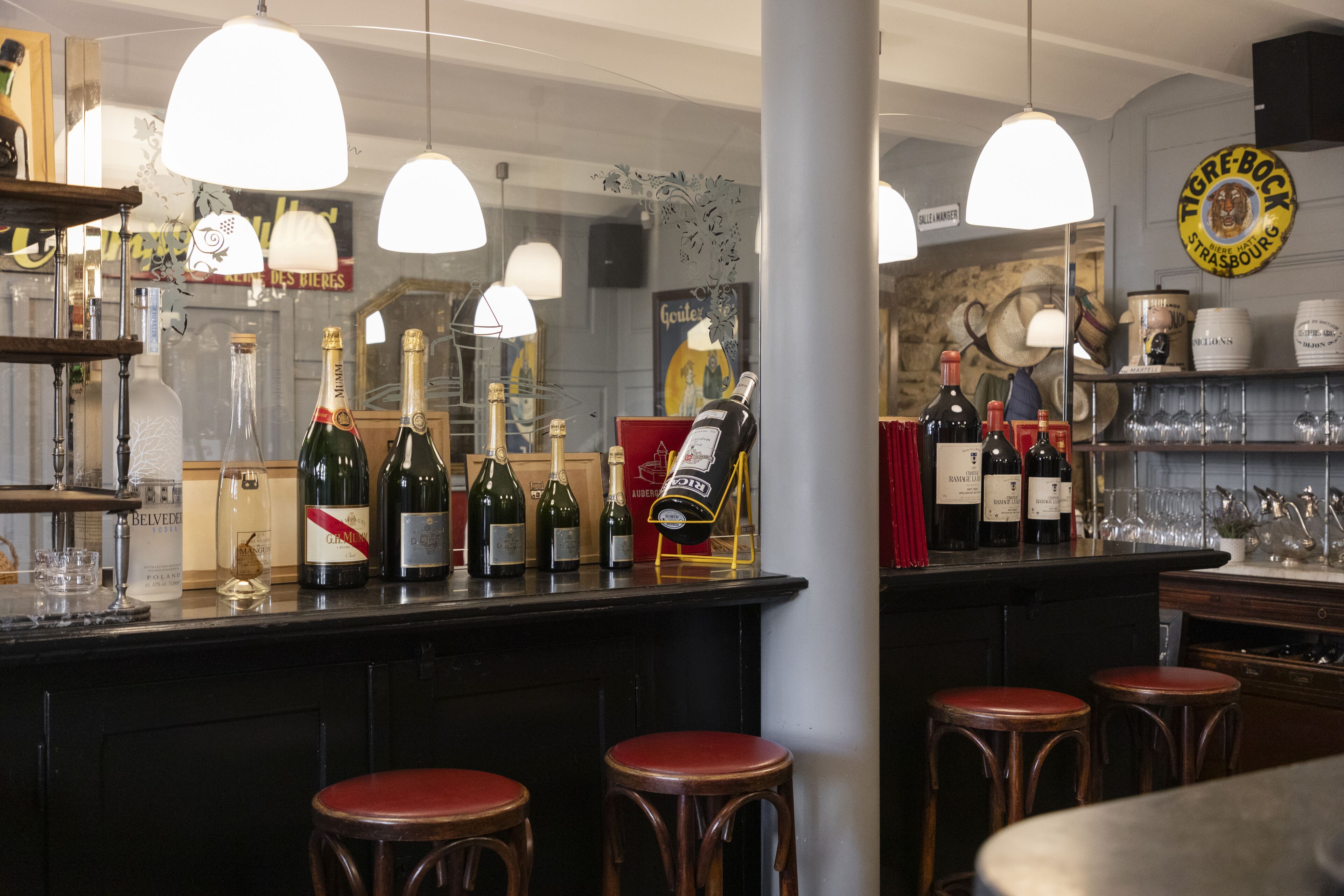 Zona de bar con varias botellas de vino y champán, taburetes de madera y lámparas colgantes.