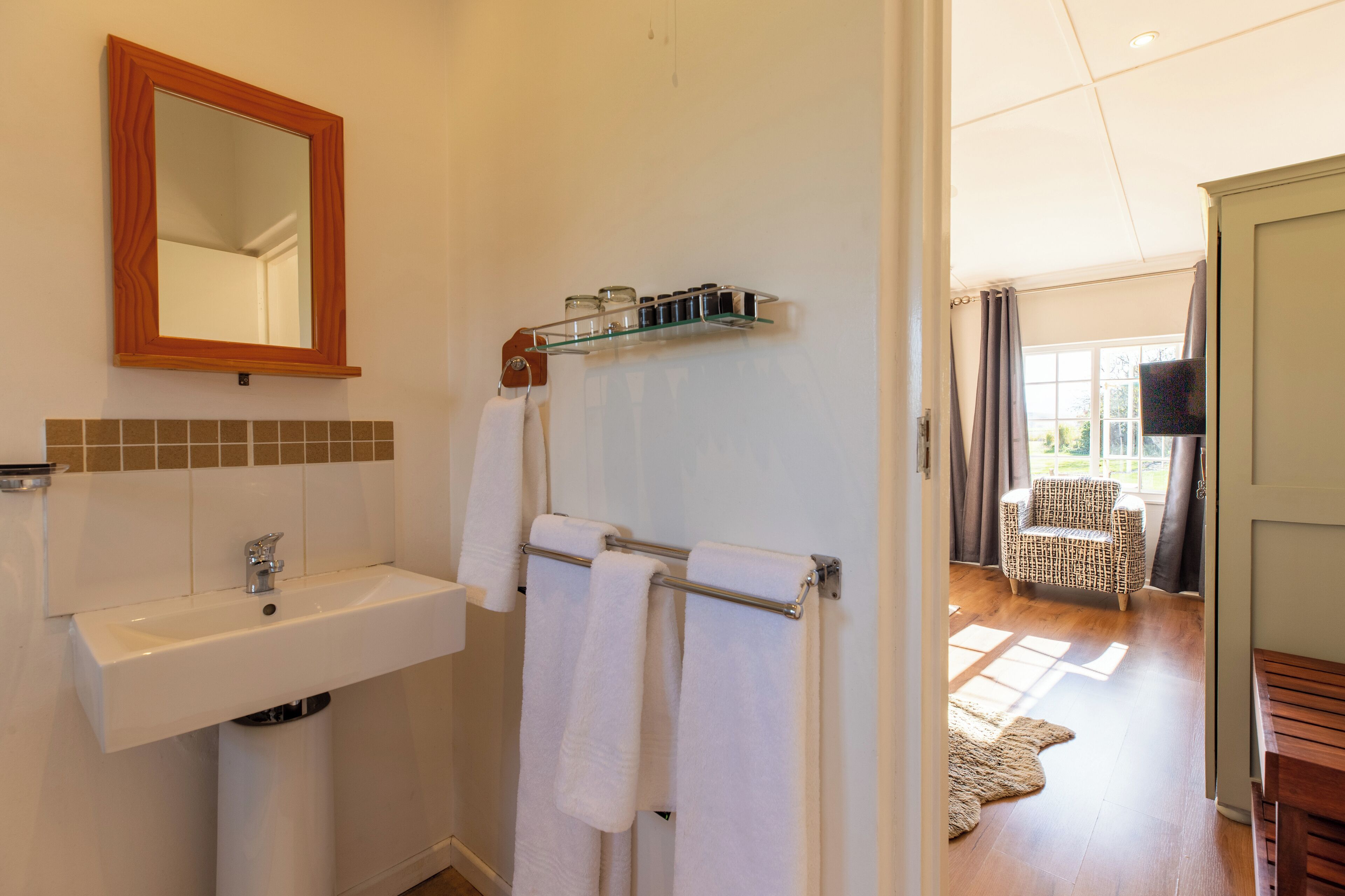 Une salle de bain équipée d’un lavabo, d’un miroir, d’un porte-serviettes et d’une fenêtre avec des rideaux.