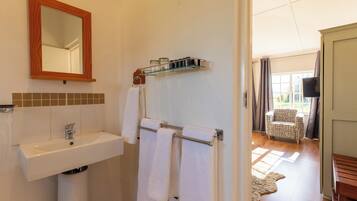 Une salle de bain équipée d’un lavabo, d’un miroir, d’un porte-serviettes et d’une fenêtre avec des rideaux.
