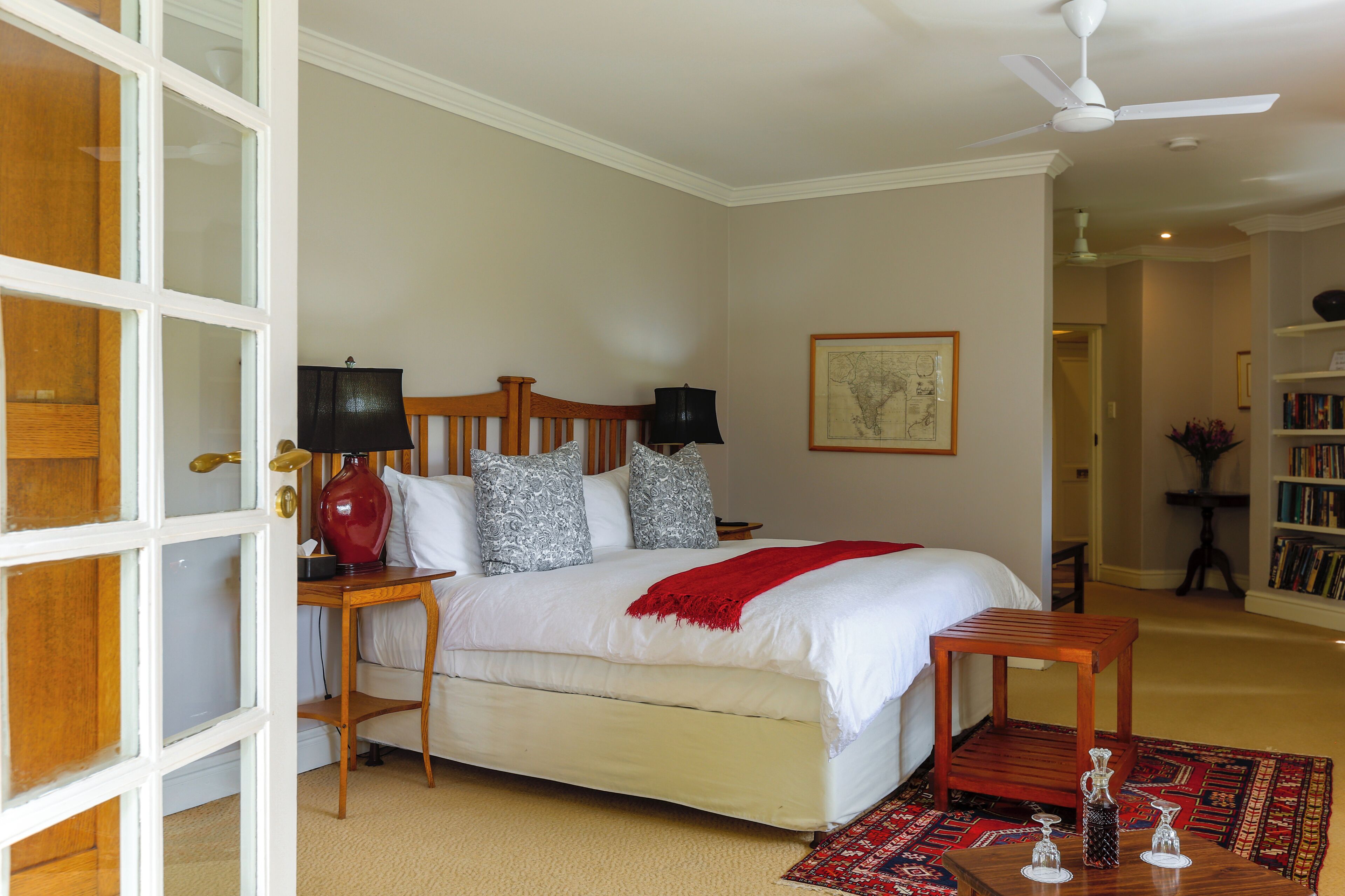 Un dormitorio con cama, mesitas de noche, una manta roja y un cabecero de madera.