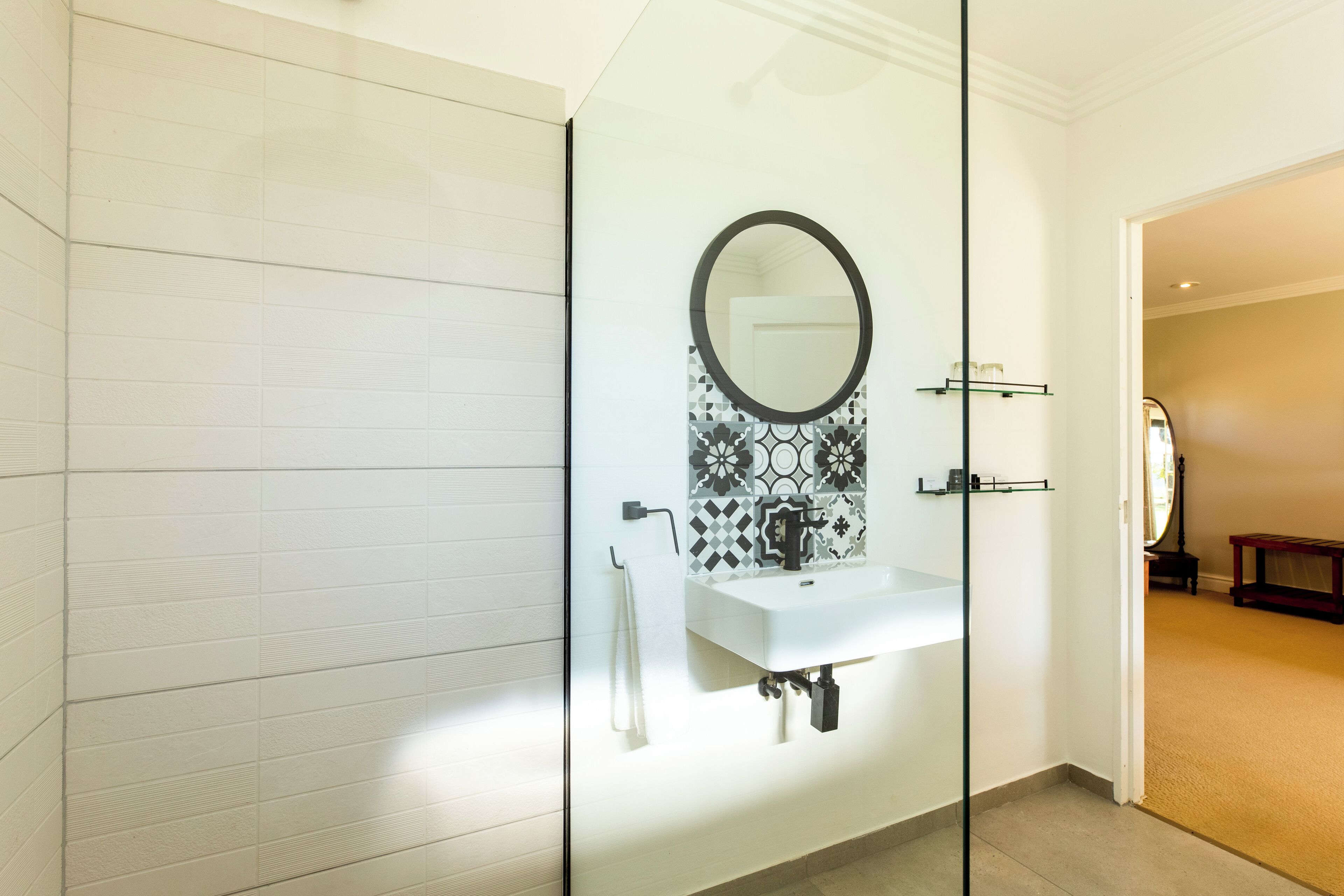 Un baño moderno con cabina de ducha de vidrio, un lavamanos blanco con grifo negro y un salpicadero decorado.