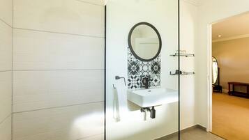 Un baño moderno con cabina de ducha de vidrio, un lavamanos blanco con grifo negro y un salpicadero decorado.