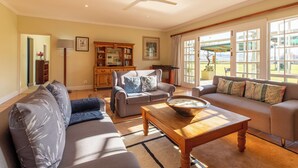 A spacious living room with a ceiling fan, two sofas, a coffee table, and a bookshelf. - Moorcroft Manor Boutique Country Hotel (Himeville)
