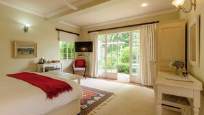 A bedroom with a bed, a desk, a chair, a television, and a window with curtains. - Moorcroft Manor Boutique Country Hotel (Himeville)