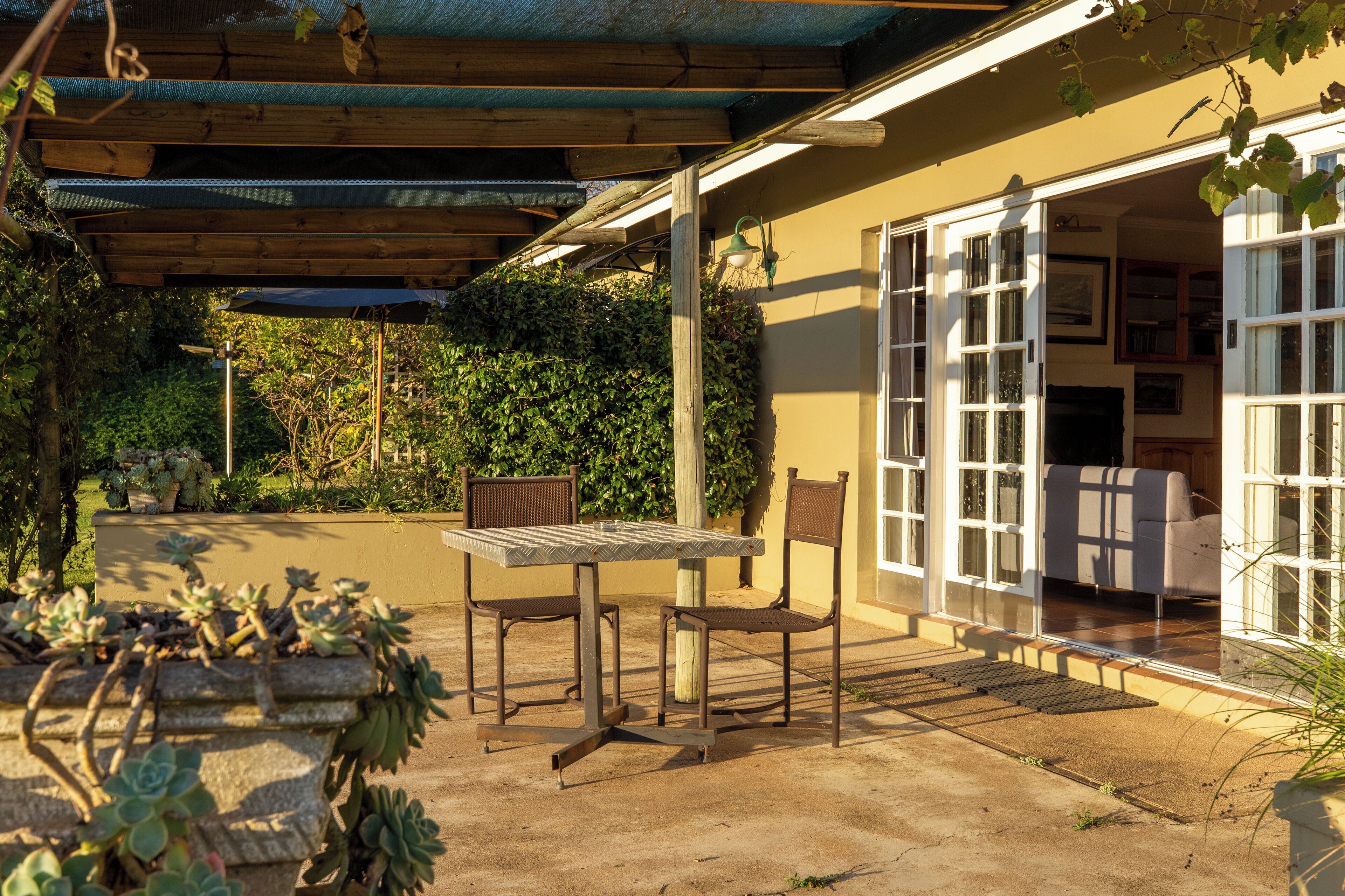 A covered patio with a table and chairs, a concrete floor, and a view of the interior through glass doors.