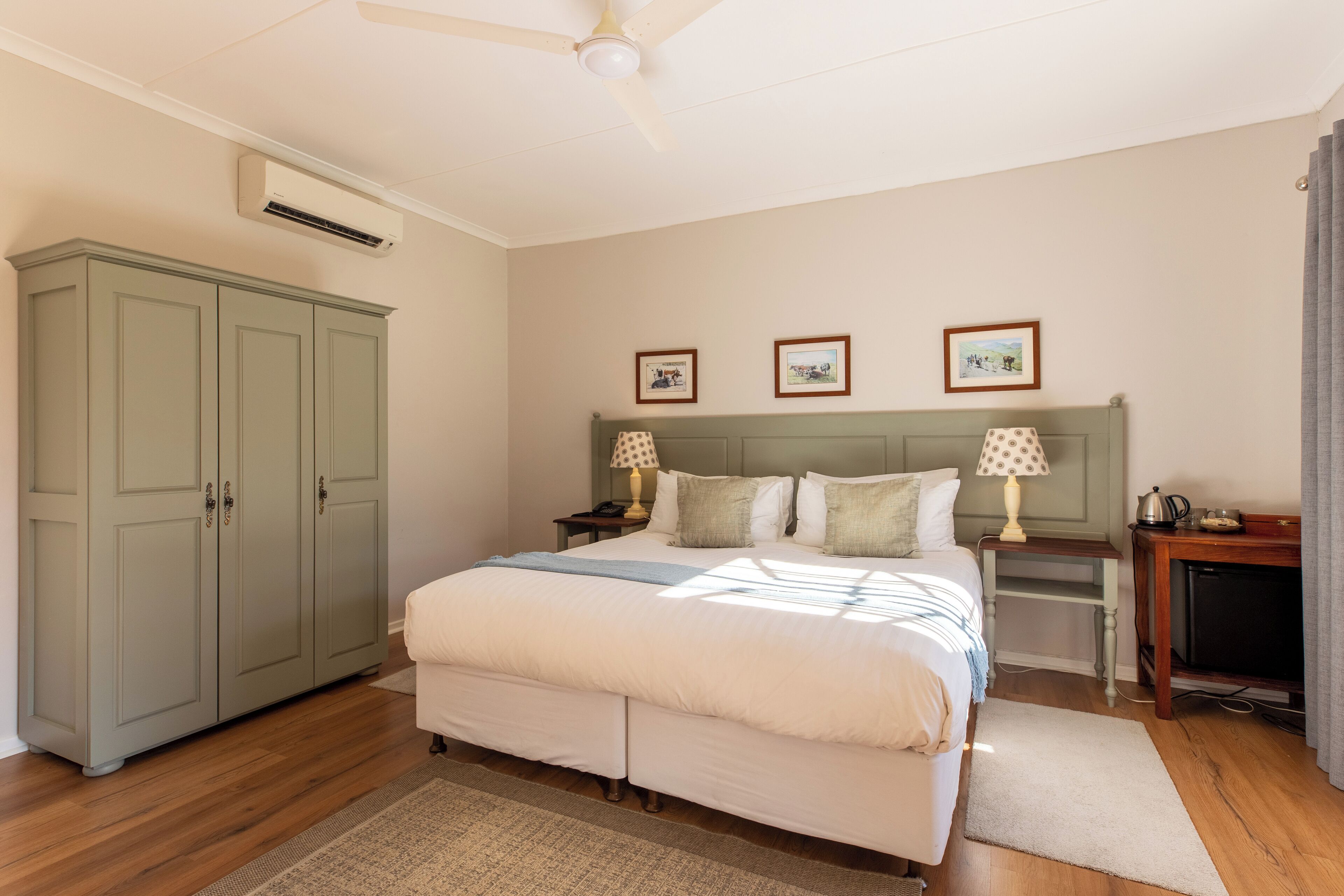 A bedroom with a large bed, a wardrobe, a nightstand, and a desk with a lamp.