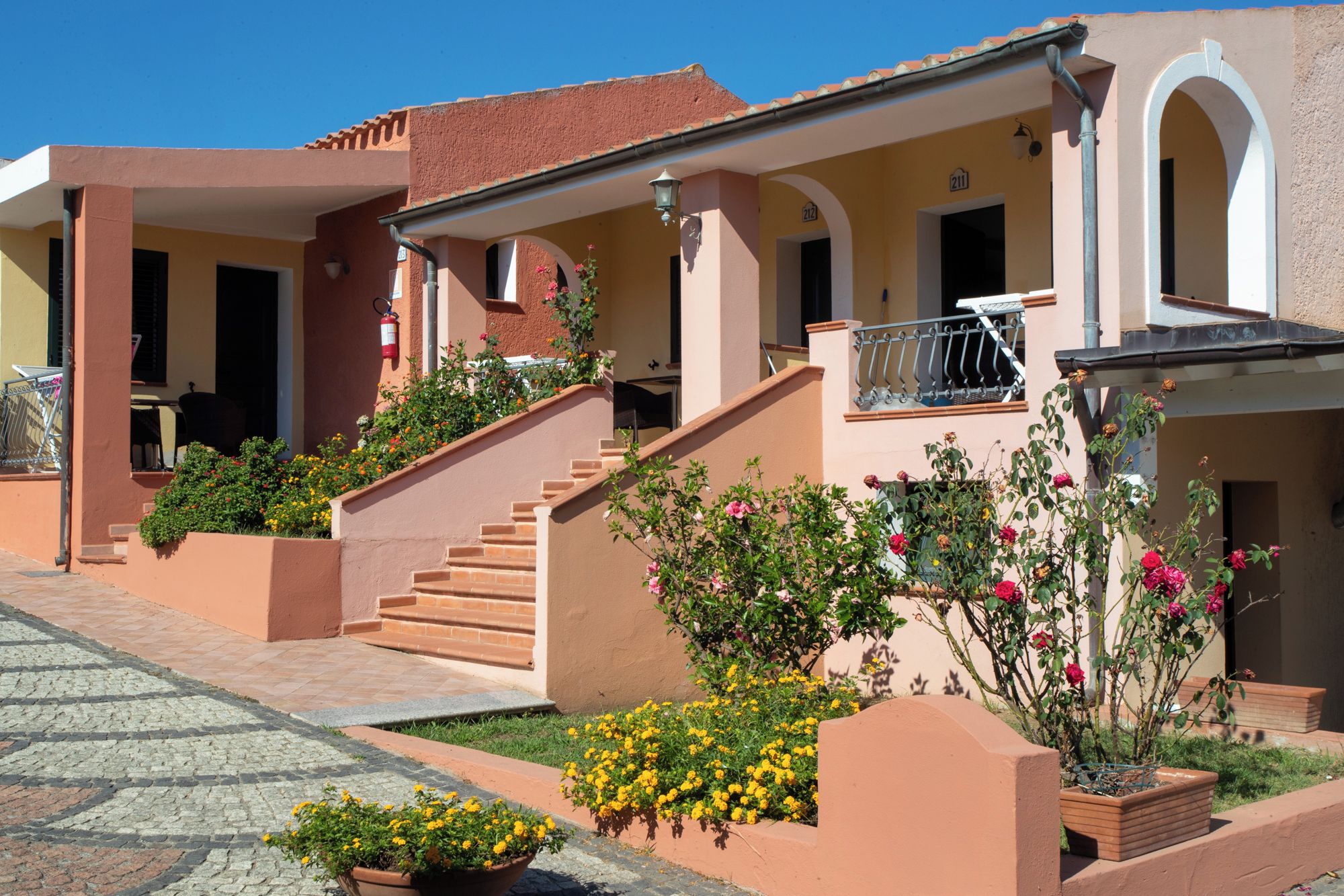 A row of Mediterranean-style buildings with stucco walls, terracotta roofs, and a paved courtyard.