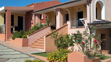 A row of Mediterranean-style buildings with stucco walls, terracotta roofs, and a paved courtyard.