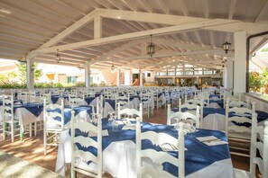 A large covered outdoor dining area with white chairs and tables, each set with blue tablecloths and white napkins. - Club Hotel Marina Seada Beach (Budoni)