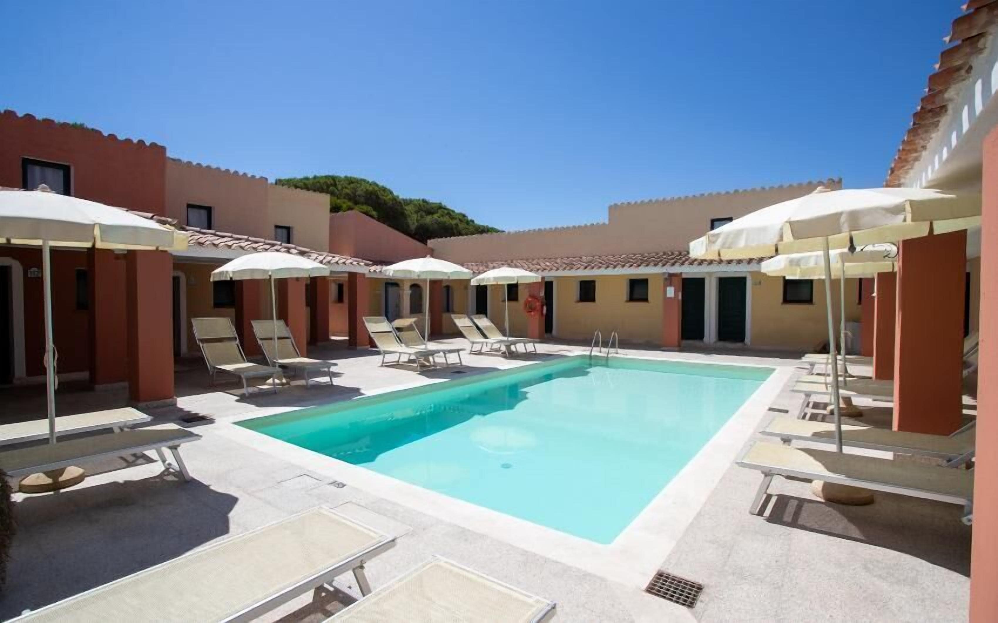 Ein Poolbereich mit Liegestühlen und Sonnenschirmen, umgeben von Gebäuden mit einheitlichem Baustil.