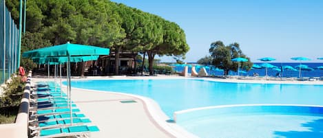 A swimming pool with lounge chairs and umbrellas, surrounded by trees and a clear sky.