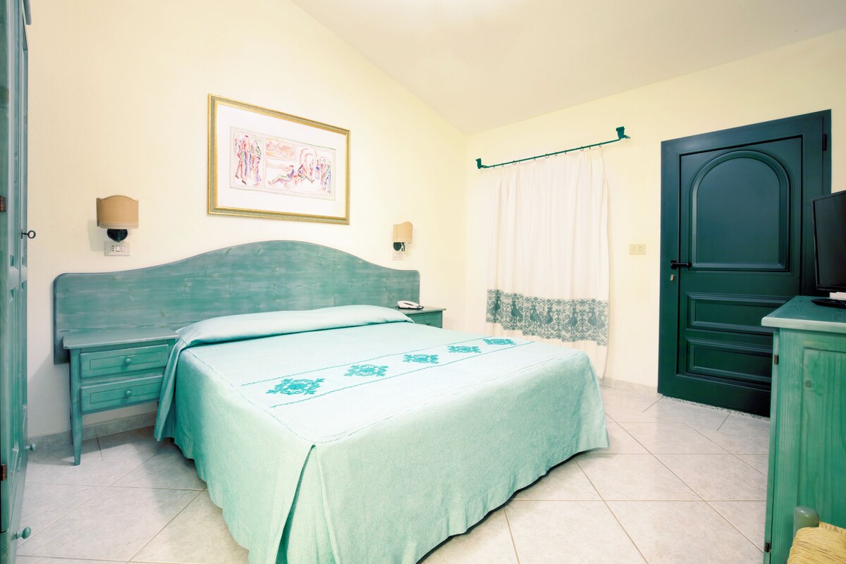 A bedroom with a bed, a nightstand, a dresser, a door, and a wall-mounted light fixture.