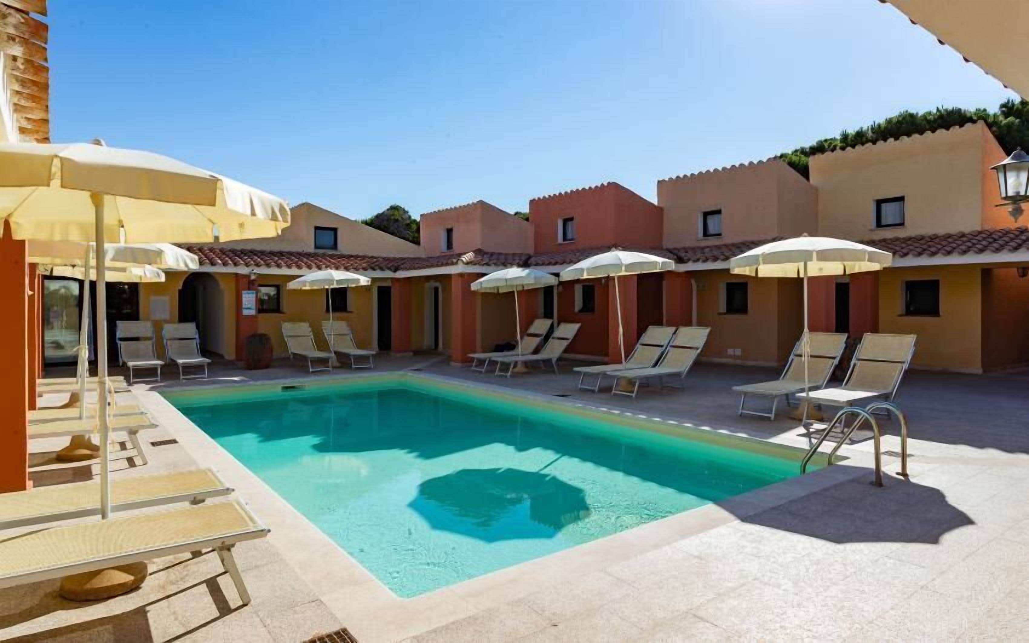 Ein Swimmingpool mit Liegestühlen und Sonnenschirmen, umgeben von Gebäuden mit Ziegeldächern.