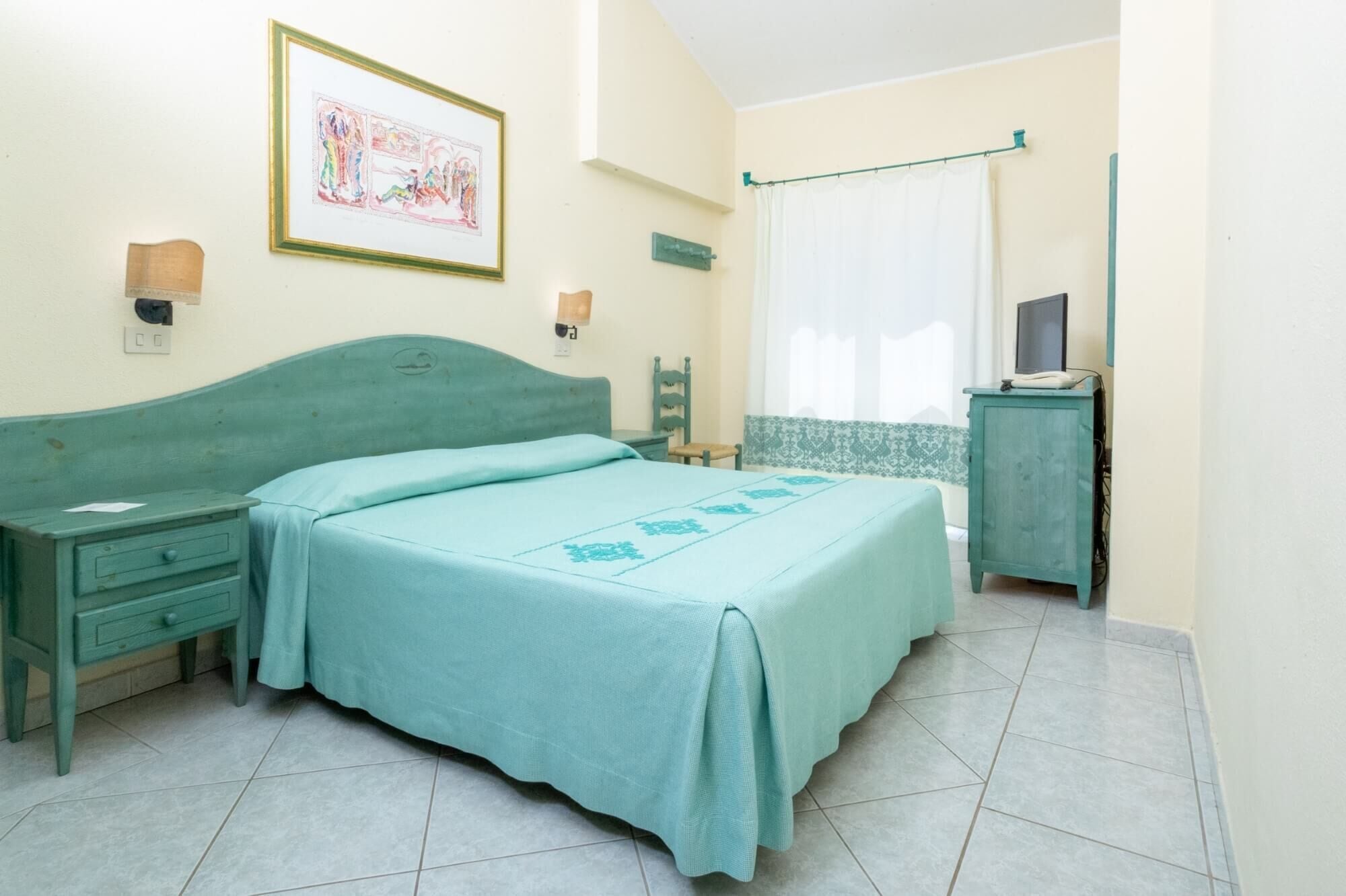 Ein Schlafzimmer mit Bett, Nachttisch, Kommode, Fernseher und einer Wandleuchte.