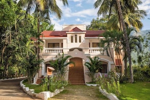 A two-story building with a red-tiled roof, a central entrance with a staircase, and a surrounding garden with palm trees. - Black Thunder (METTUPALAYAM)
