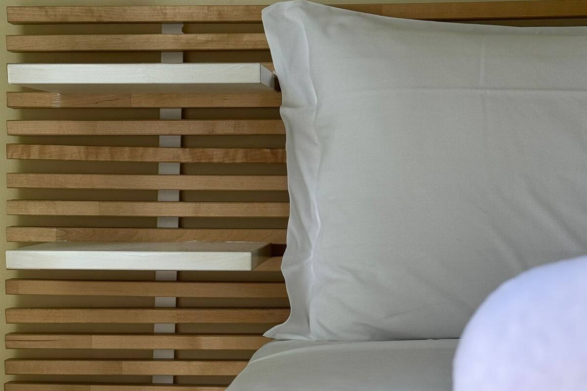 Una cama con cabecera de listones de madera y almohada blanca.
